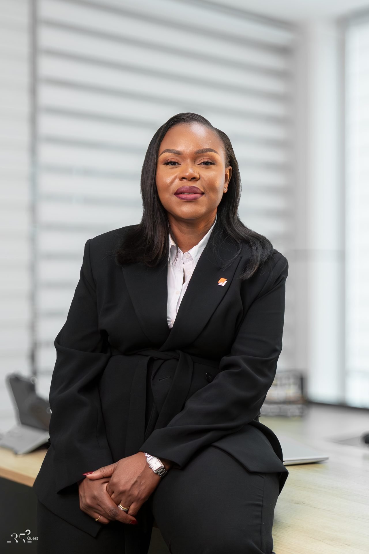 Audrey Koffi Niamkey assise sur le rebord d’un bureau, en tenue noire.
