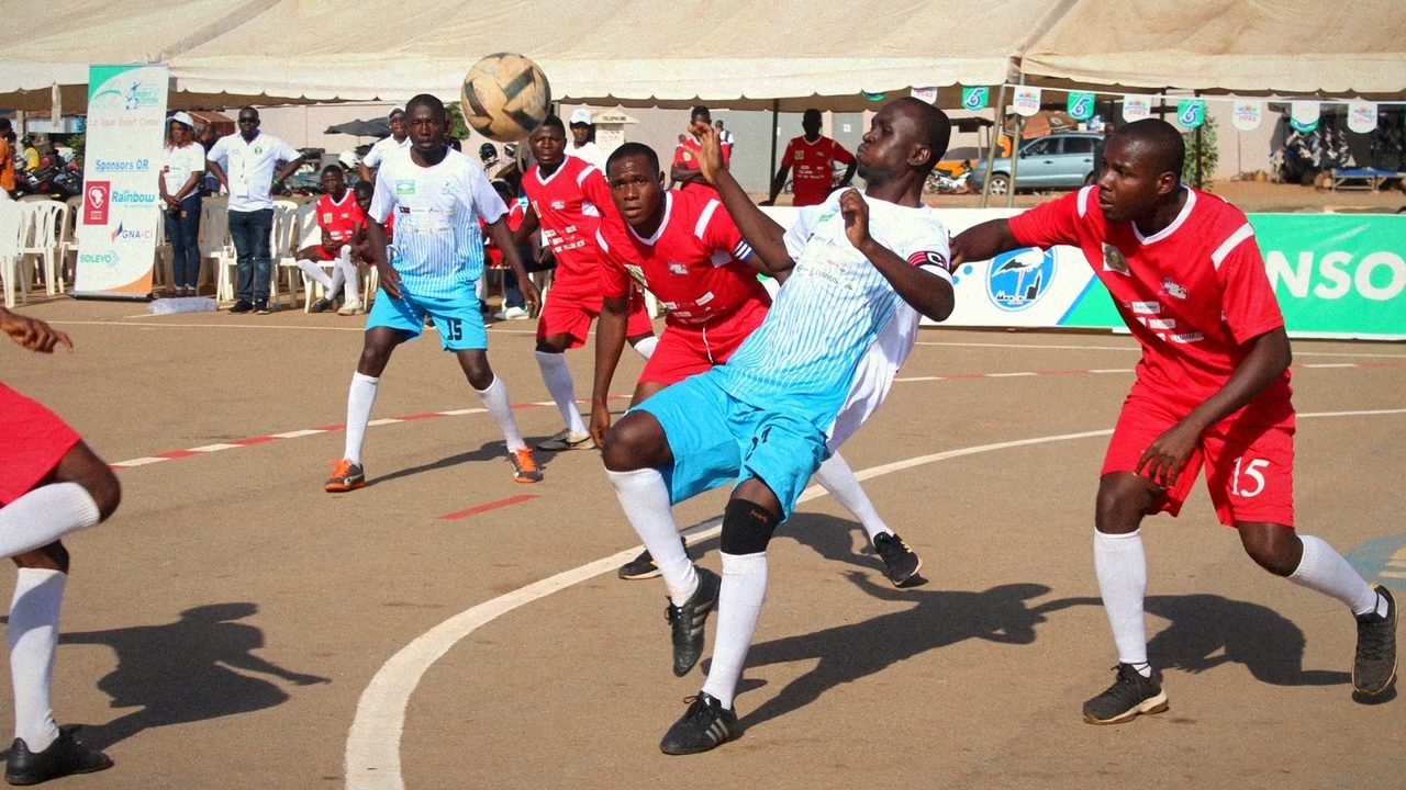 Match de maracana de la Ligue Sport Coton : un joueur en maillot bleu clair contrôle le ballon face à des joueurs en rouge.